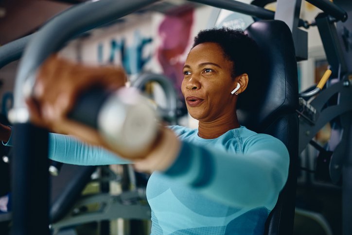 Black sportswoman doing chest exercises on machine while working out in gym.