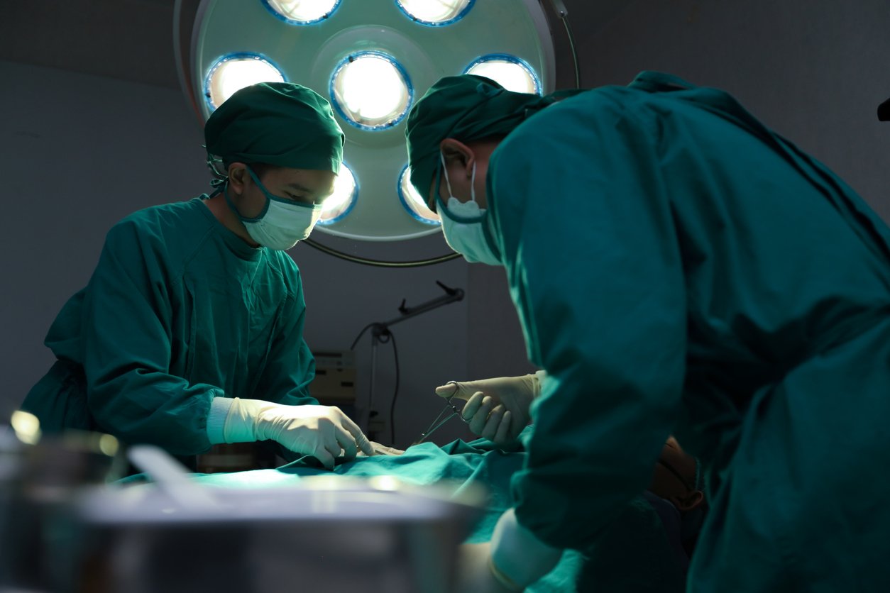 Closeup image of professional concentrated surgical team hands performing an operation with patient in hospital operating room. Surgery concept. Surgical Management of Repeated Pilonidal Disease